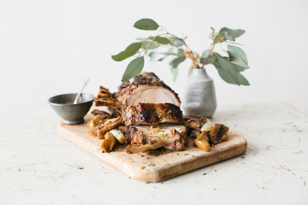 Maple Crusted Rack of Pork with Roasted Apples and Shallots on a wooden cutting board with a plant behind it 