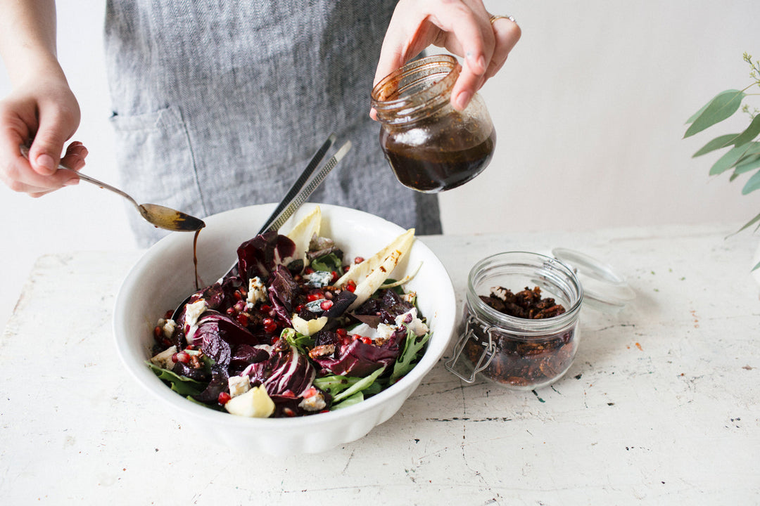 Winter Beet and Pomegranate Salad with Maple Mustard Candied Pecans in a white bowl being drizzled with salad dressing
