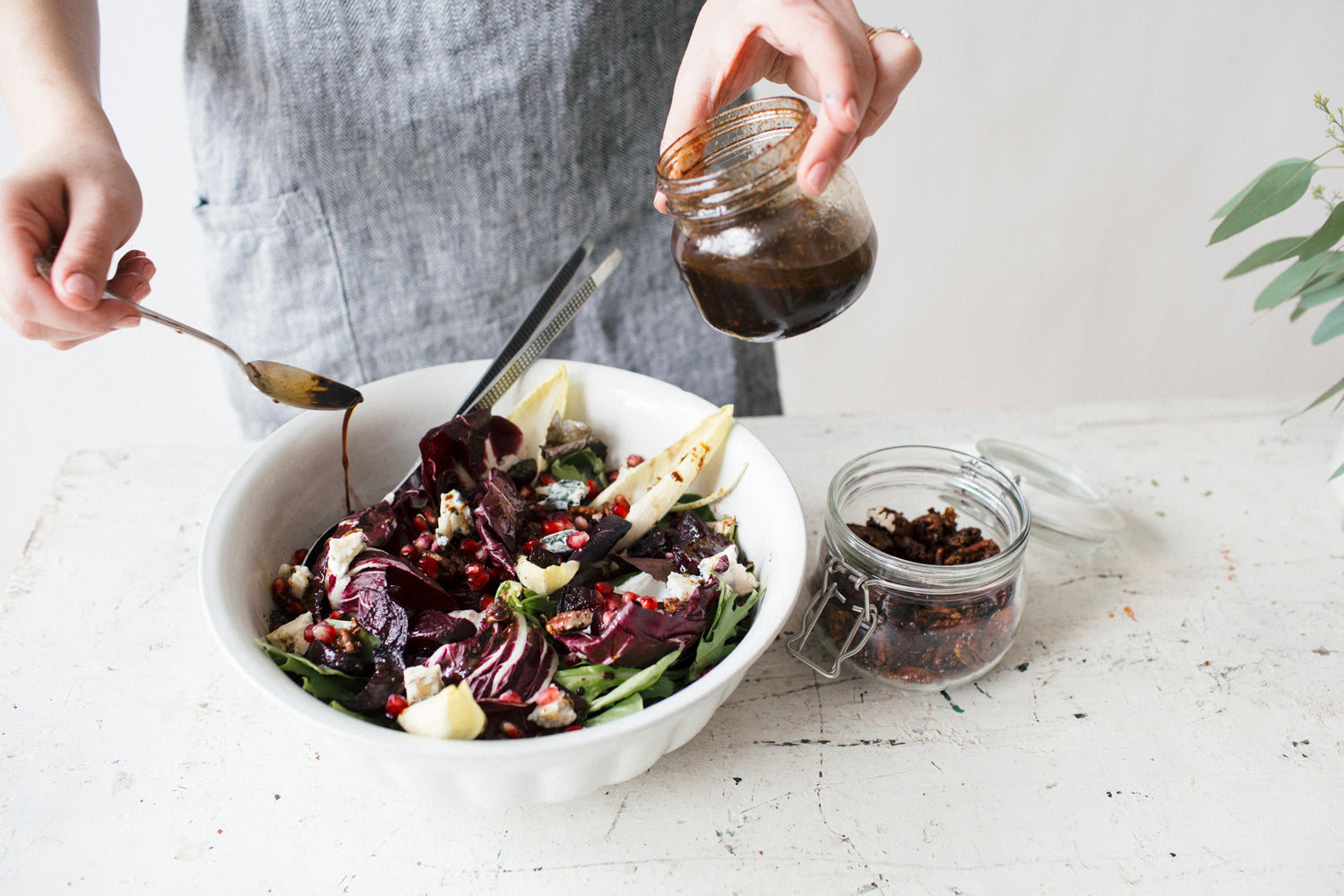 Winter Beet and Pomegranate Salad with Maple Mustard Candied Pecans in a white bowl being drizzled with salad dressing