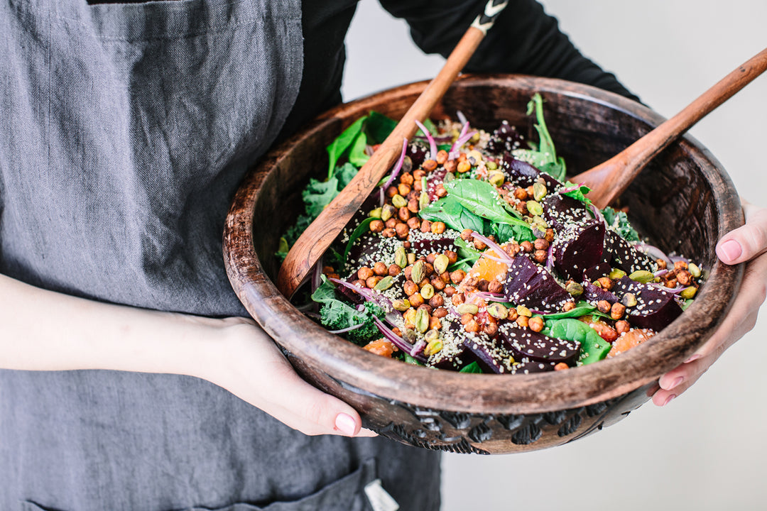 A woman holding the Superfood Citrus Salad with Crispy Chickpeas, Blood Oranges, and Beets in a wooden bowl with wooden salad tossers