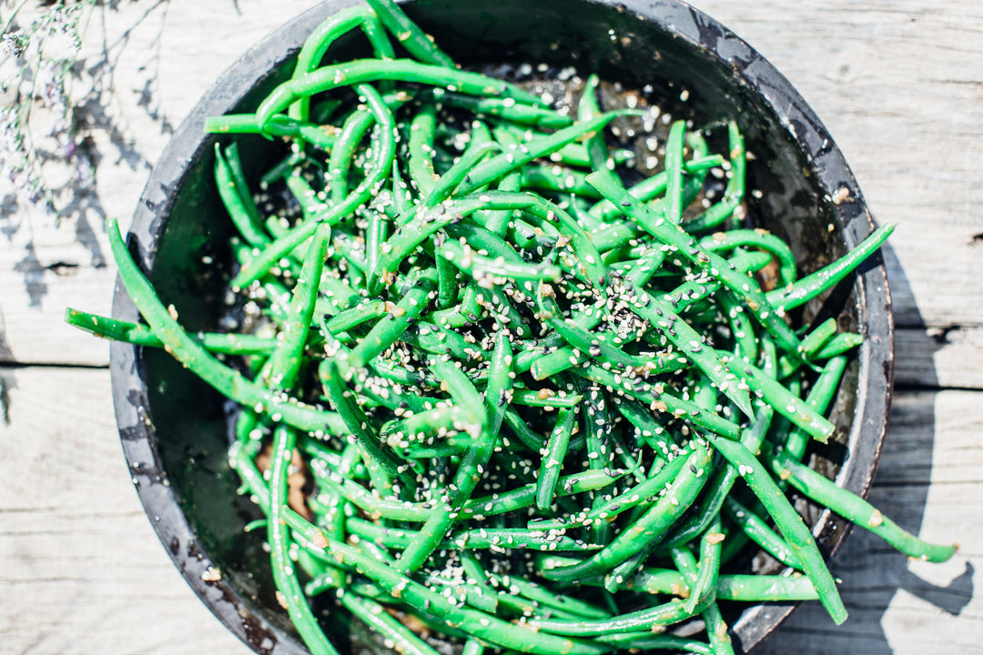 Garden Green Beans with Ginger and Sesame Dressing in a black bowl placed on a wooden picnic table