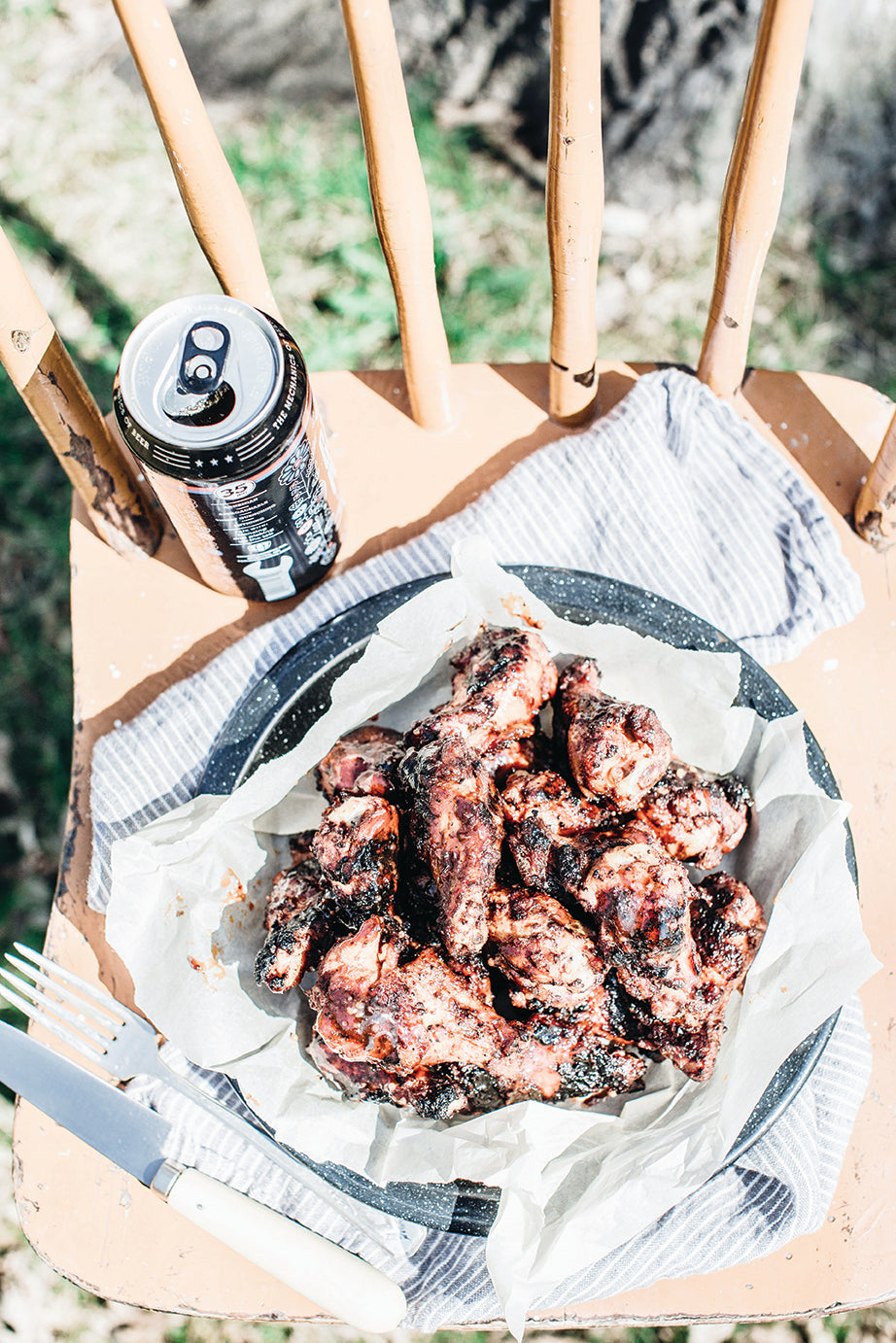 Sweet + Smoky Grilled Beer Wings in a basket on a wooden chair with a beer beside it