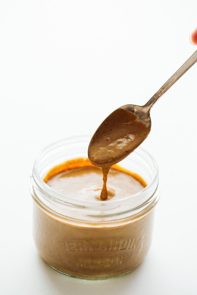 Balsamic Tahini Dressing being spooned out of a mason jar