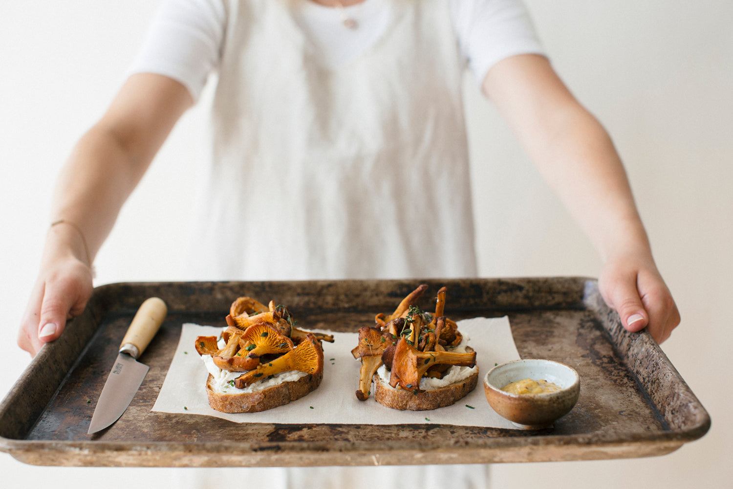 A woman holding a a worn pan with 2 pieces of mushroom and whipped ricotta toast on top of it 