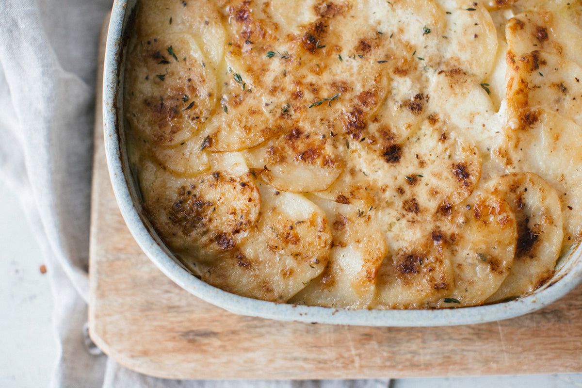 Creamy Potato Gratin in a white ceramic dish on a wooden board