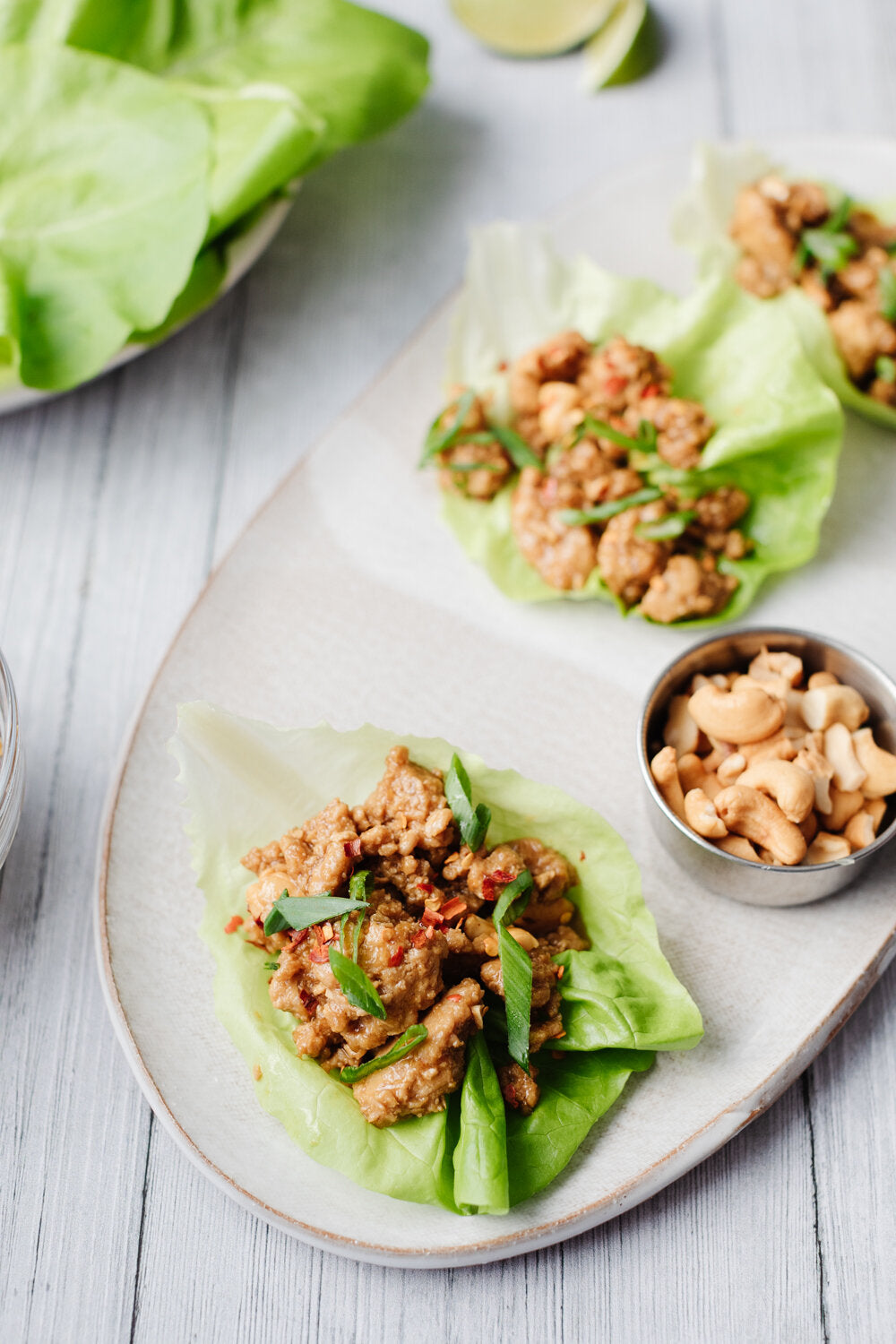 Two Spicy Cashew Chicken Lettuce Wraps on a serving plate with a side dish of cashews beside it