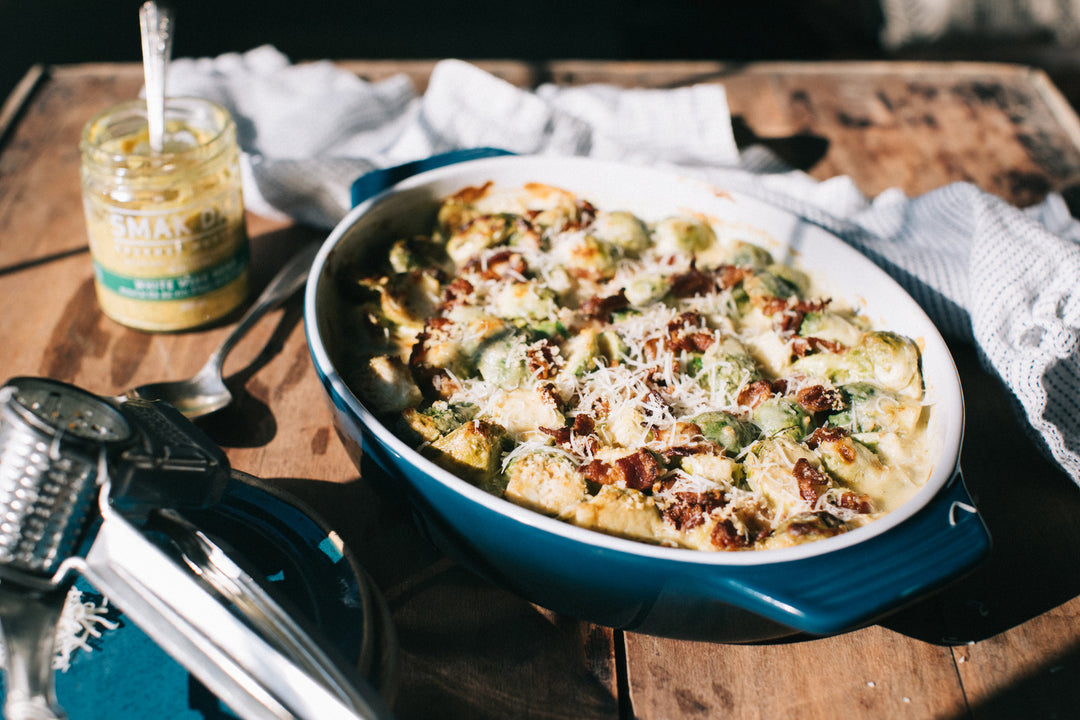 Creamy Brussels Sprouts + Bacon Gratin in a blue baking dish on a table