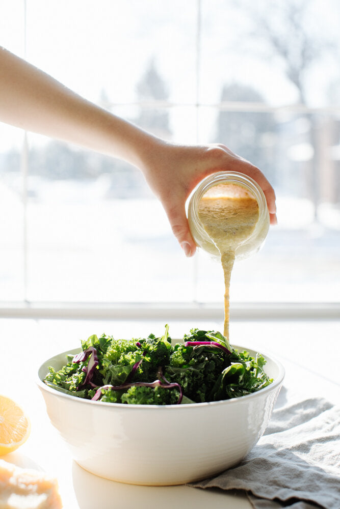 Lemony Hummus Caesar Dressing being drizzled over a green salad in a white bowl