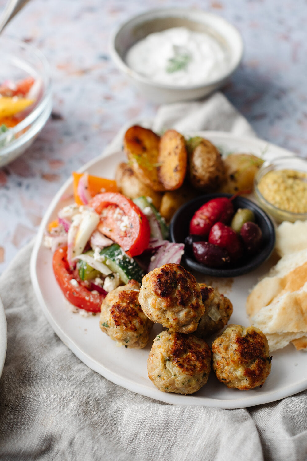 A full greek plate with greek salad, potatoes, olives, and Pan Seared Lemony Greek Turkey Meatballs