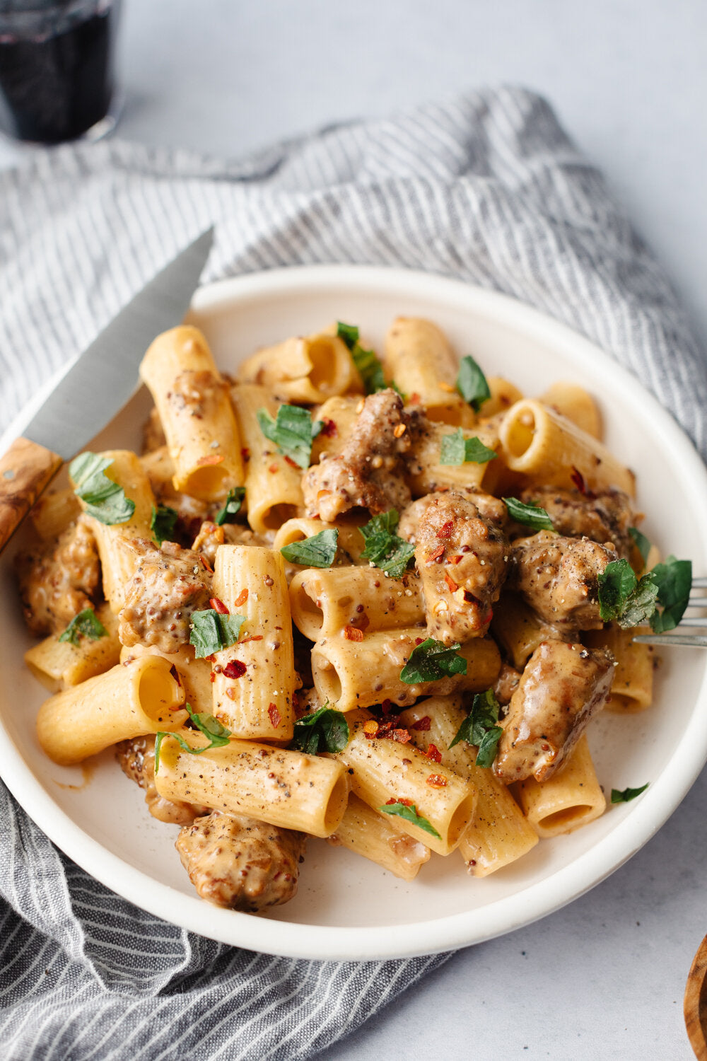Spicy Sausage Penne with Mustard Cream Sauce on a white plate on a stripped cloth