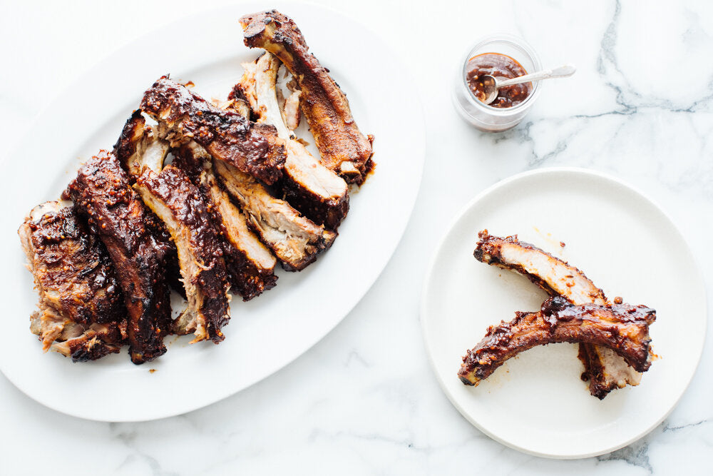 Saucy Crock-Pot BBQ Ribs on a white serving plate beside a side plate with two individual ribs