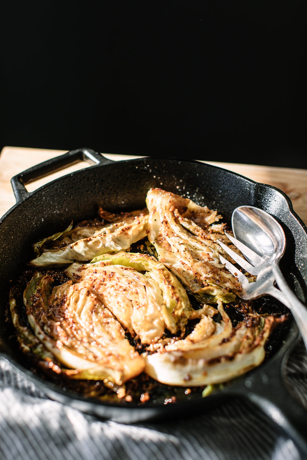 Oven roasted maple mustard cabbage in a black cast iron pan with silver serving cutlery 