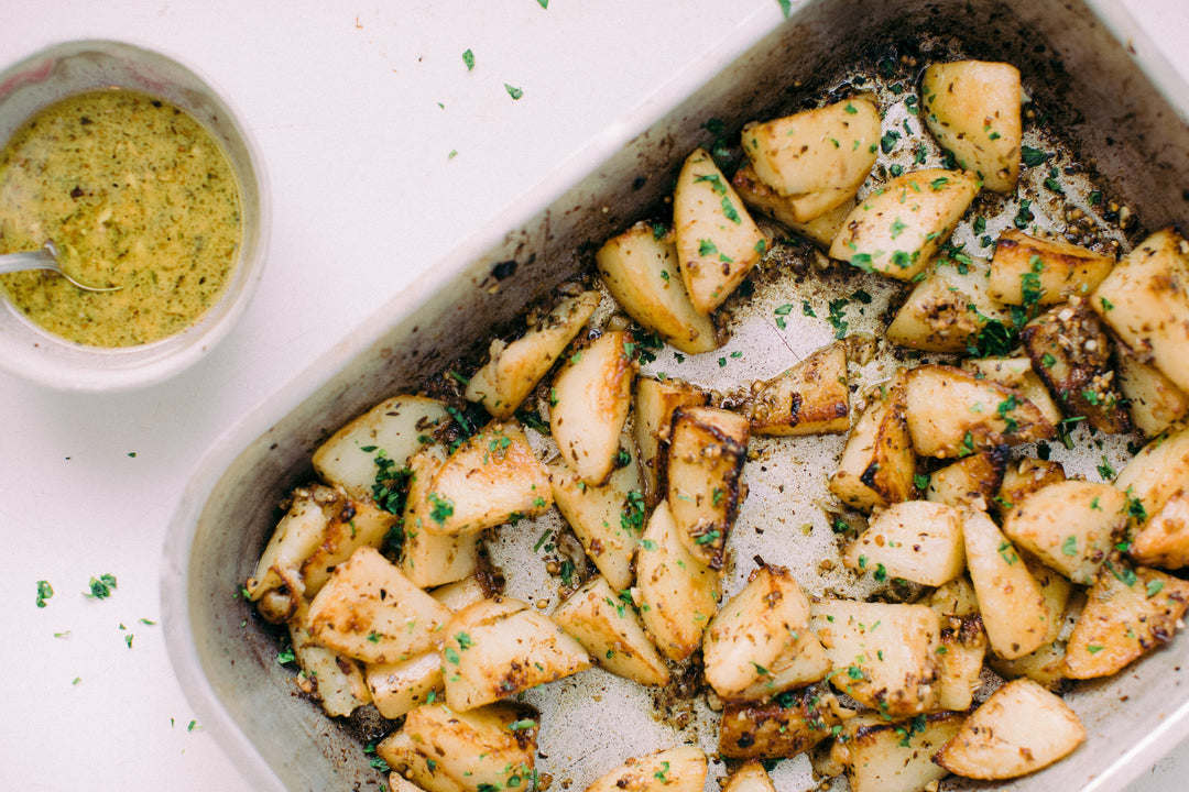 Lemony greek roasted potatos in a baking tray with a side bowl of grainy mustard