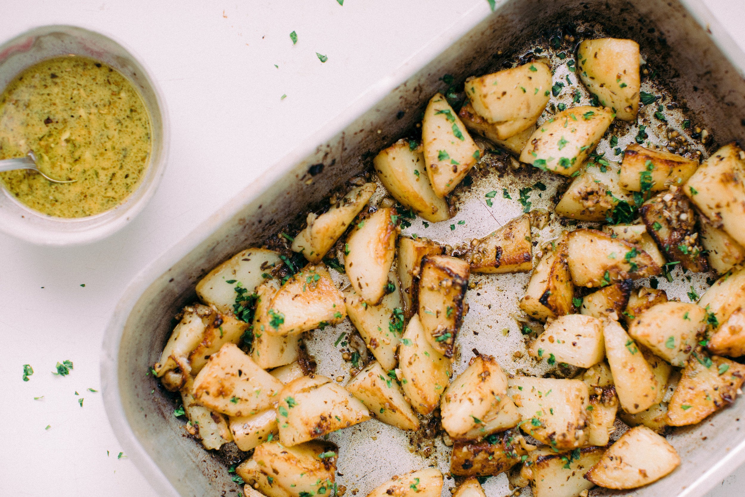 Lemony greek roasted potatos in a baking tray with a side bowl of grainy mustard