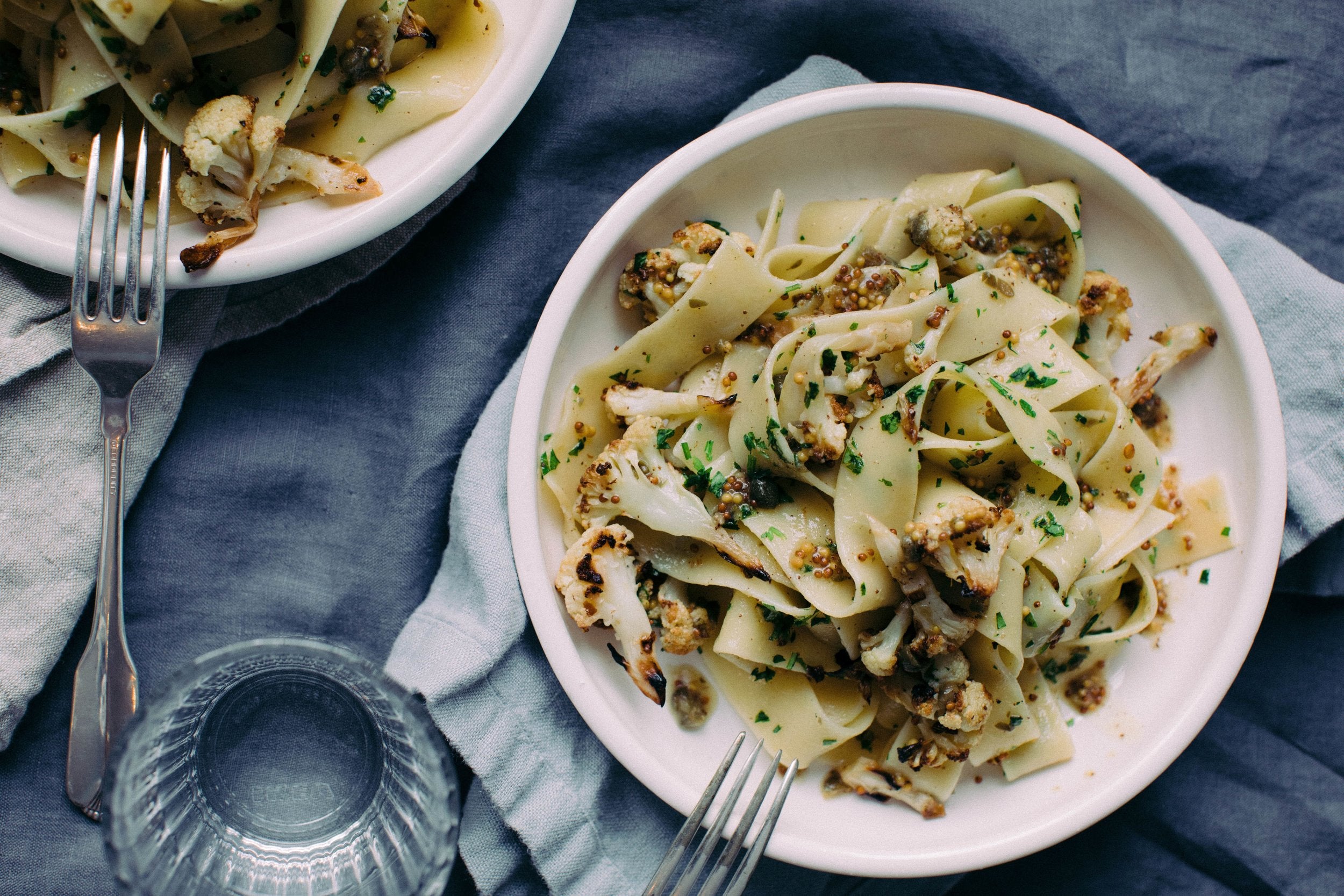 Roasted Cauliflower Pasta with Browned Butter Mustard Caper Sauce on a white plate placed on a dark blue table