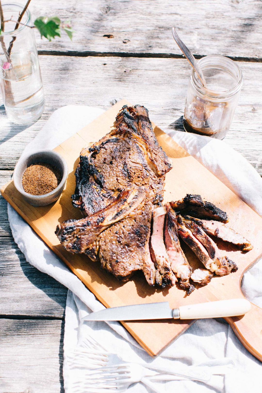 a sliced marinated rib steak on a wooden board placed on an outdoor picnic table