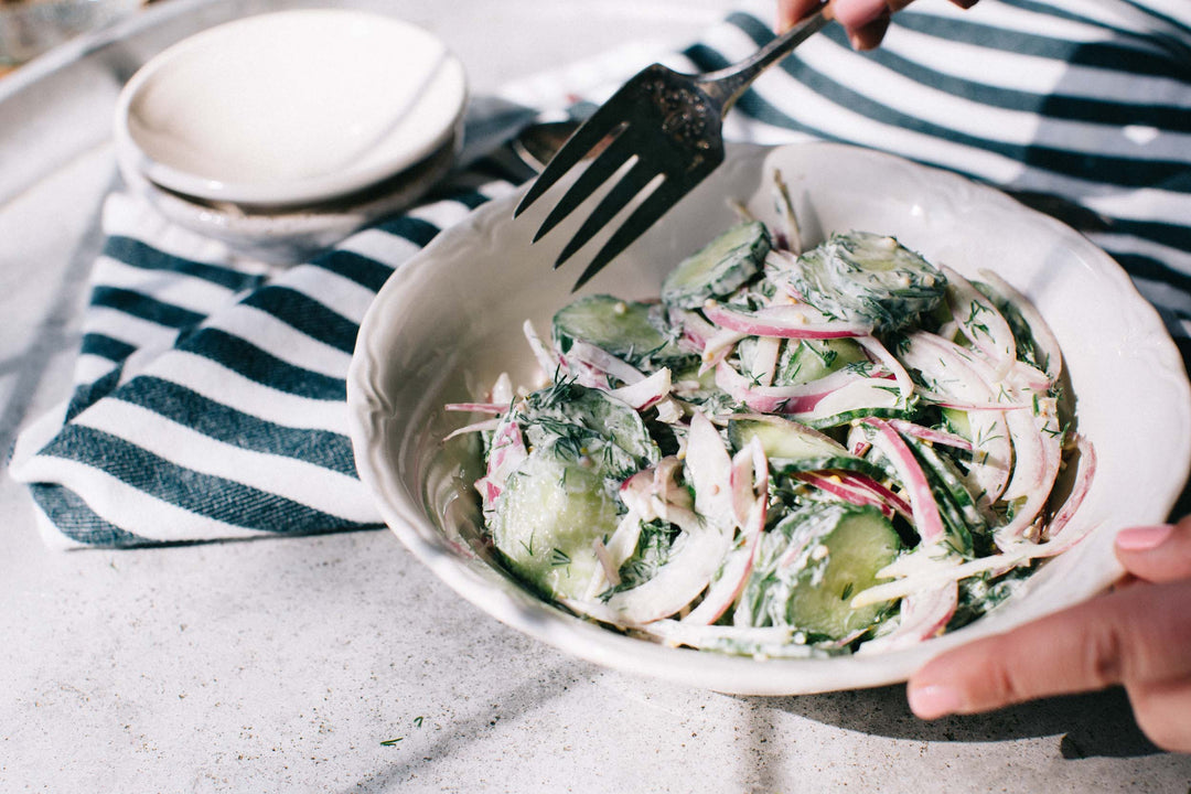 Creamy Cucumber Dill Salad with red onion on a blue and white striped kitchen towel