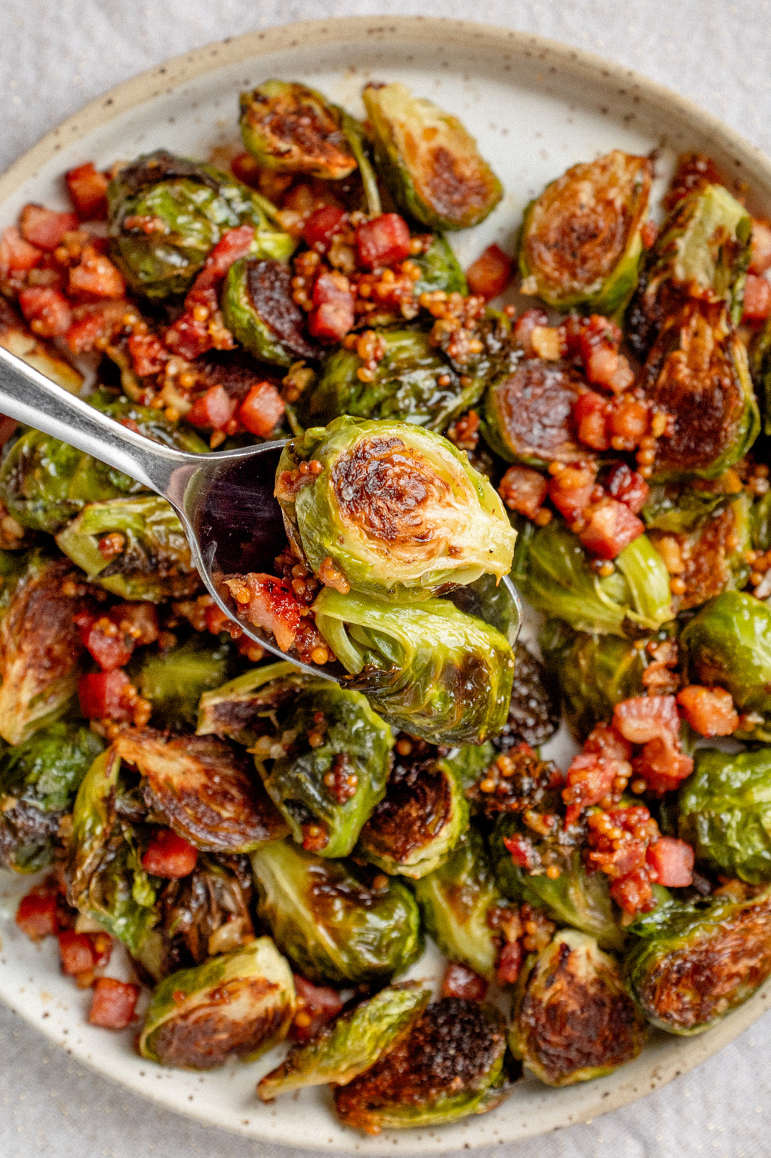 A spoonful of Brussel sprouts tipped with a pancetta vinaigrette on a speckled white plate