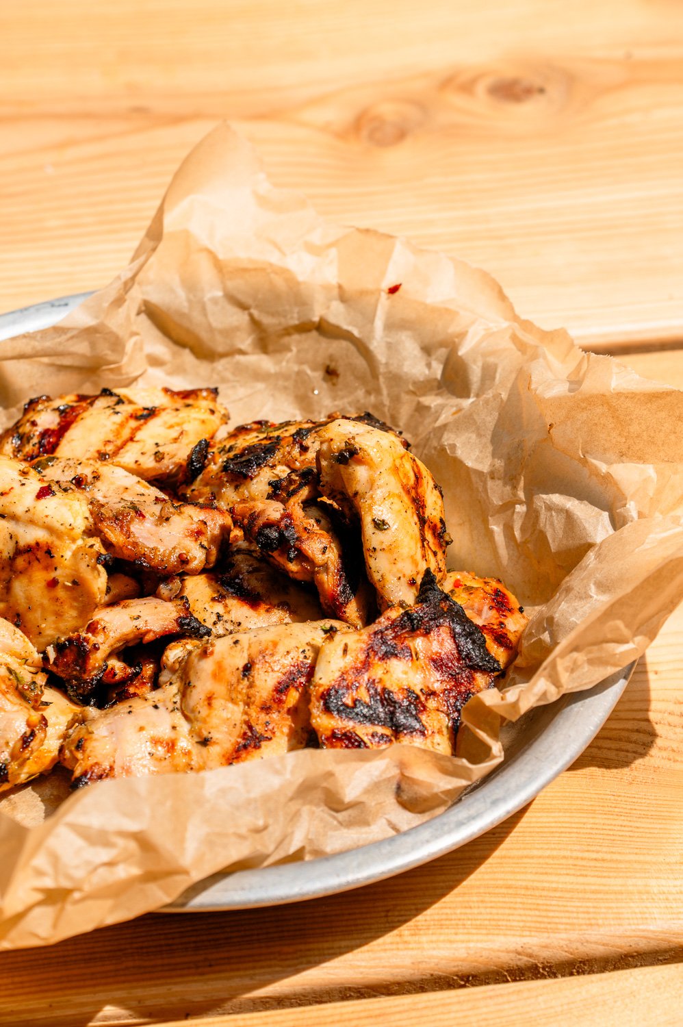 Citrus Marinated BBQ Chicken in a sliver pan with parchment paper on top a picnic table