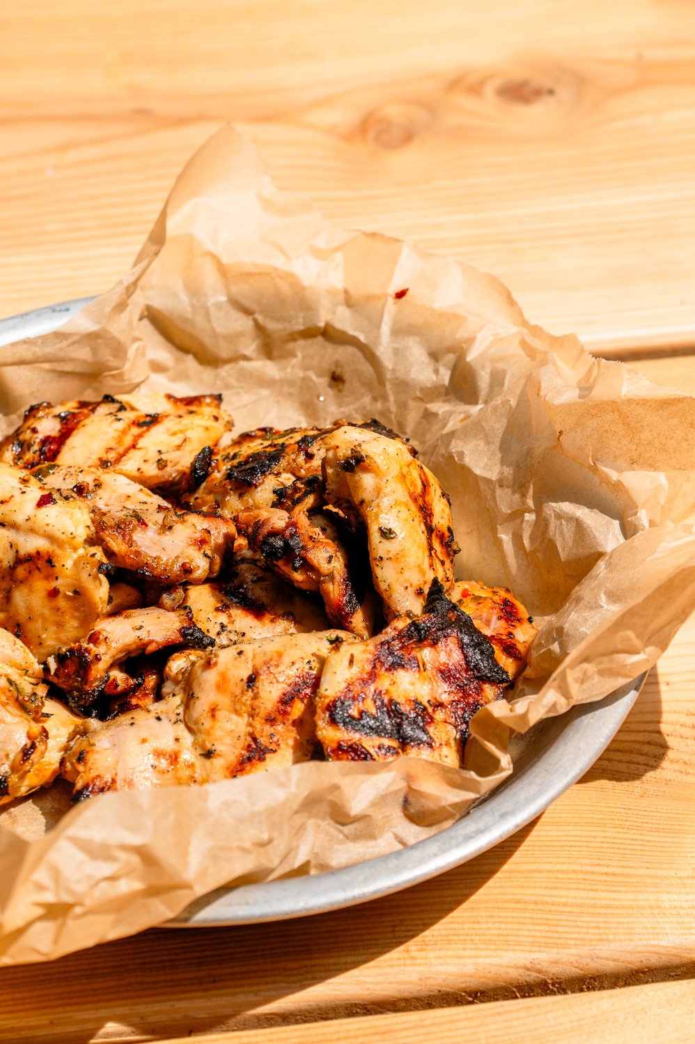 Citrus Marinated BBQ Chicken in a sliver pan with parchment paper on top a picnic table