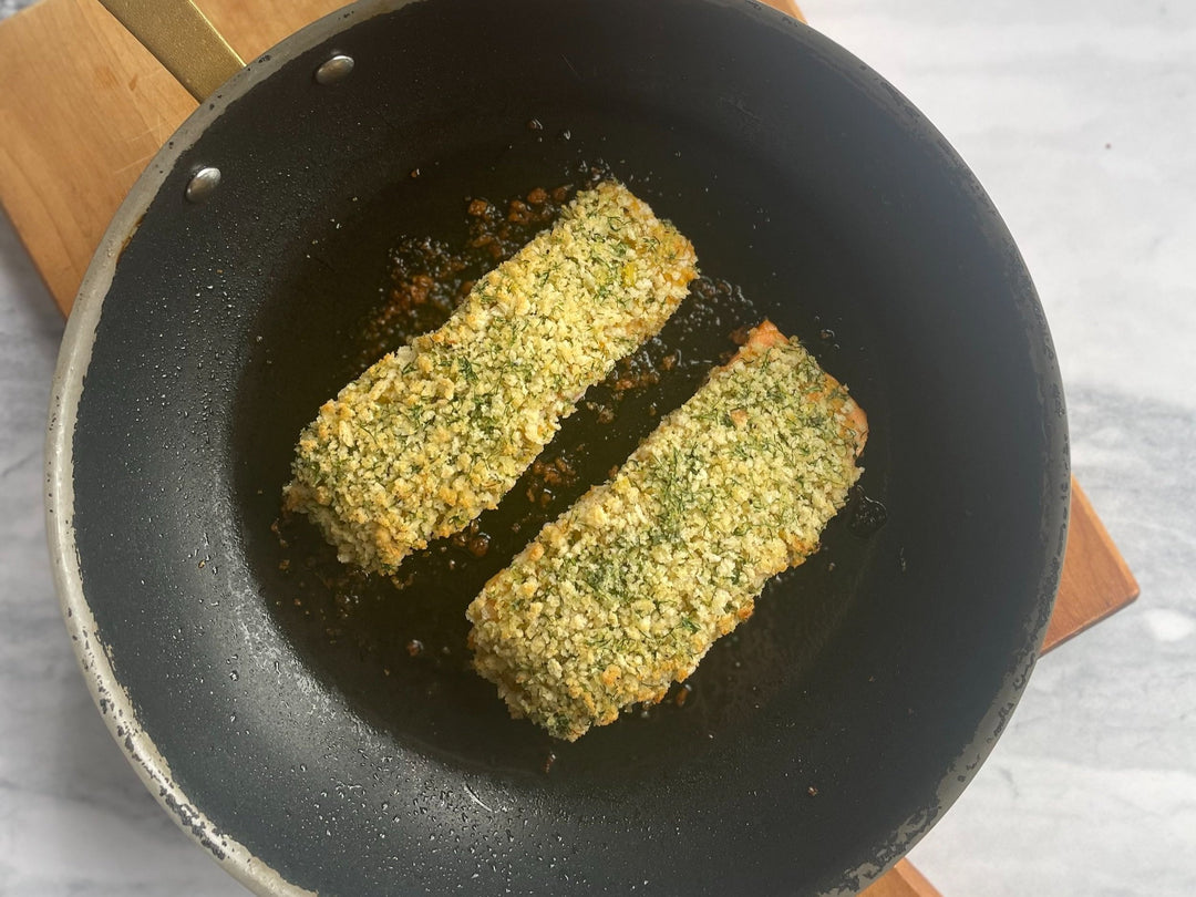 2 fillets of Panko and Herb Crusted Salmon in a frying pan on top of a wooden board