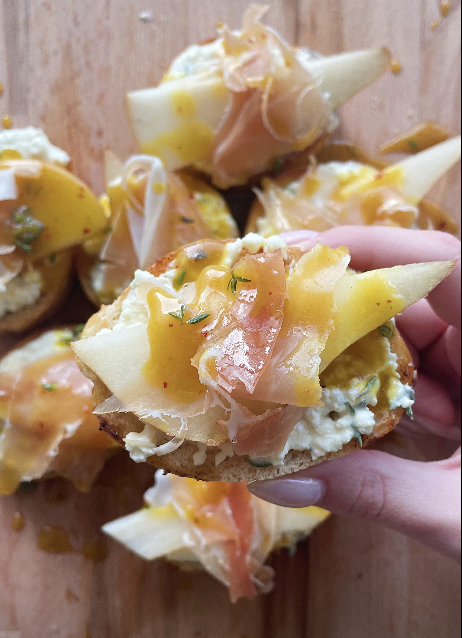 Woman's hand holding a pear and prosciutto toast over a wooden board