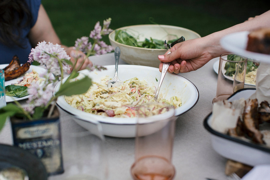 Shredded Carrot Slaw with Curry Dijon and Pistachios in a white bowl on a table with a bunch of other picnic dishes and flowers