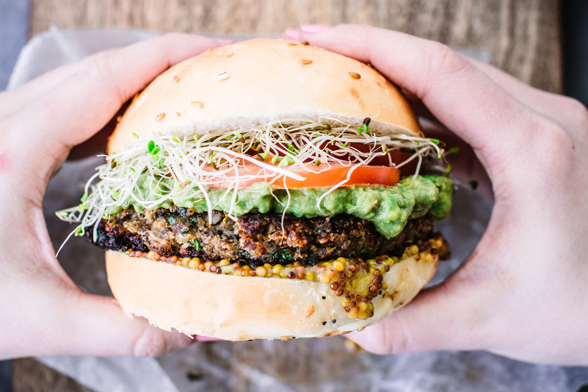 Hands holding the mushroom quinoa burger over a wooden board